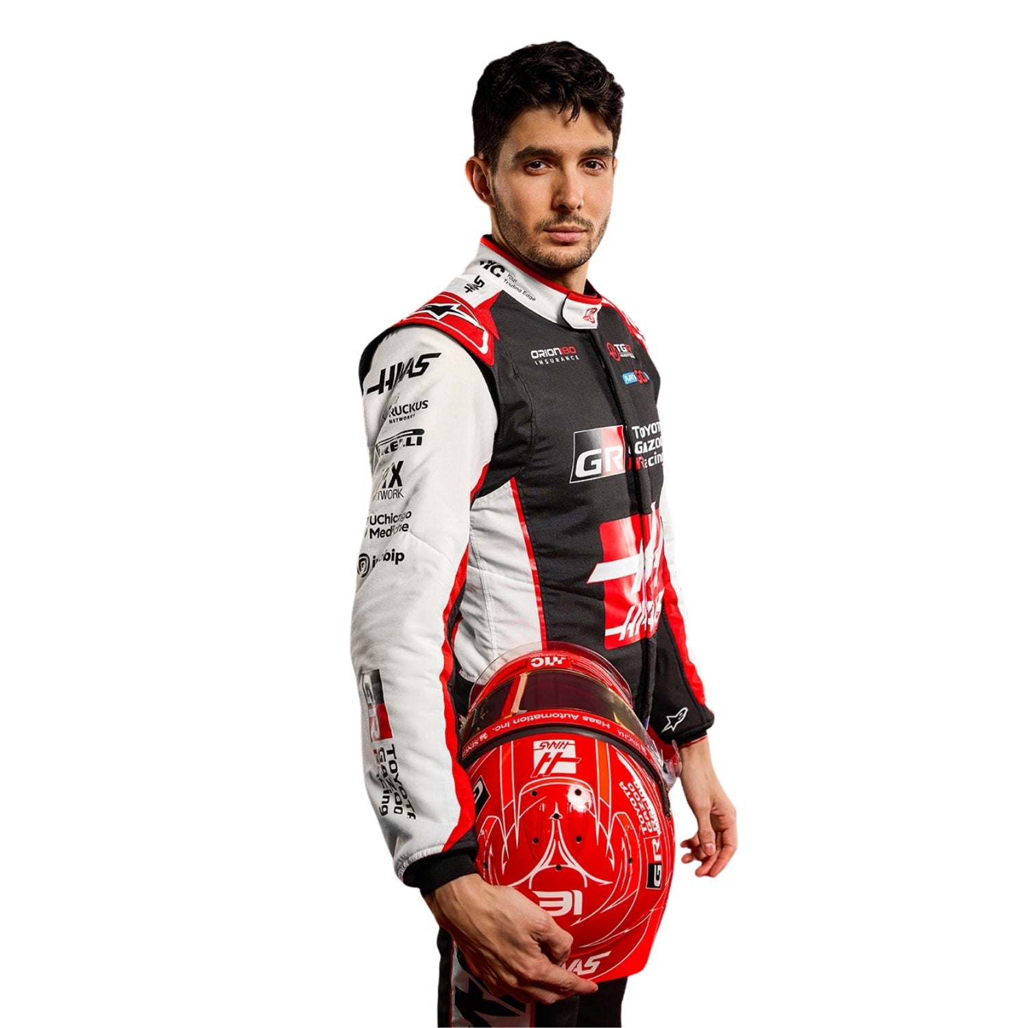 Esteban Ocon is wearing a F1 Haas 2026 racing suit and holding a helmet with various sponsor logos - Kartx Gear