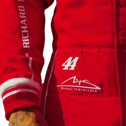 Close-up of a red racing suit with white embroidered details, including the number 44, Michael Schumacher signature, and 'RICHARD' on the sleeve, worn by a tattooed driver.